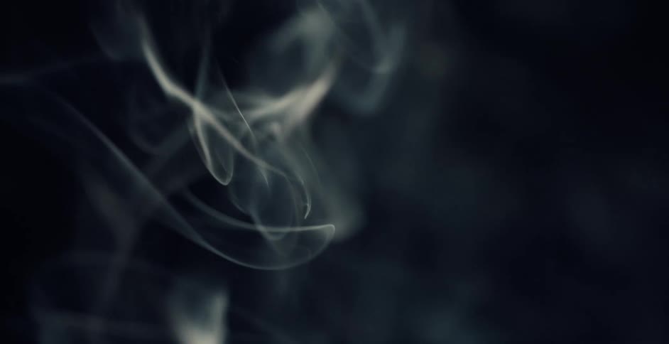 Light shines on wisps of smoke wavering as it rises in the darkness
