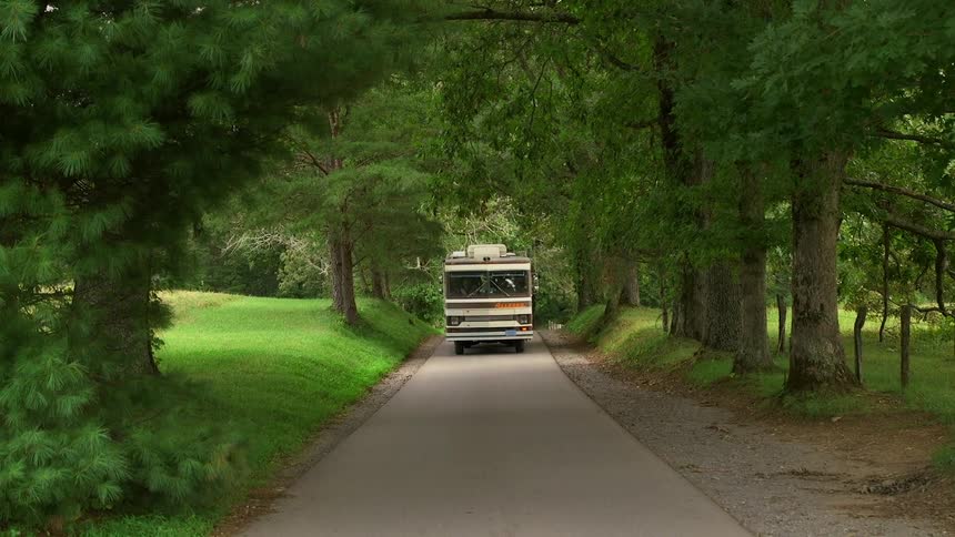 An rv drives down a tree-lined road