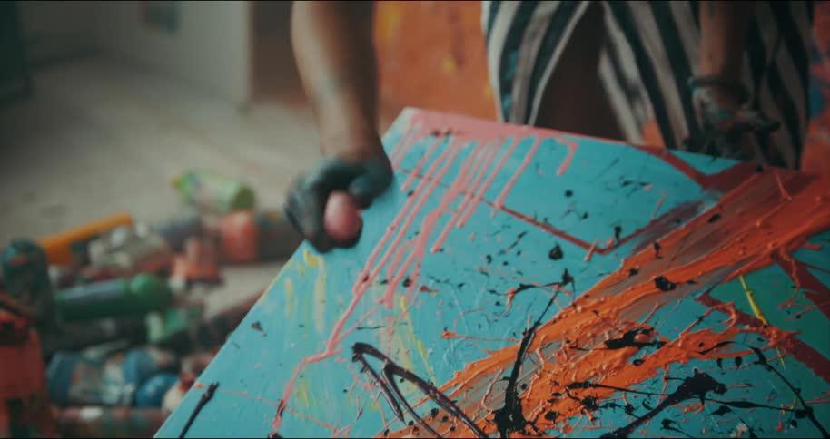 A woman is standing in a room creating a painting by splashing paint on the canvas
