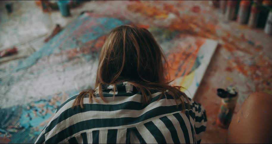 Female artist leans painting on canvas lying on a flat surface stained with paint