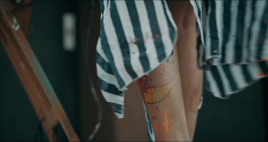 A striped smock blows open showing the paint splattered legs of an artist standing near an easel