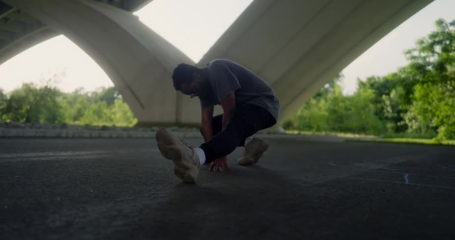 A man holding a stretch with one leg out in front of him under an overpass on a sunny day