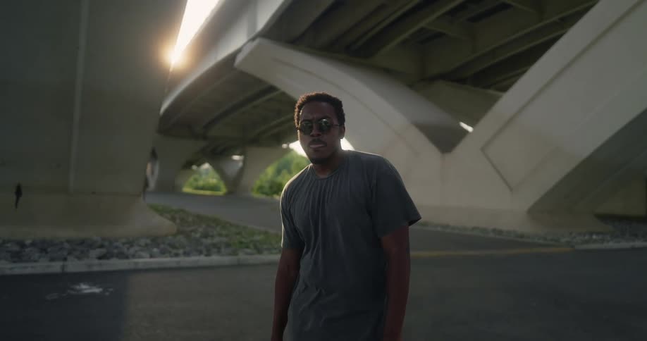 A man standing in the street under a highway overpass with sunglasses on