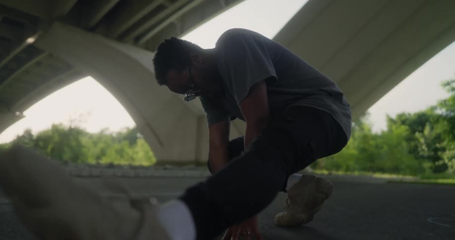 Man wearing sunglasses stretches out under a highway at daytime