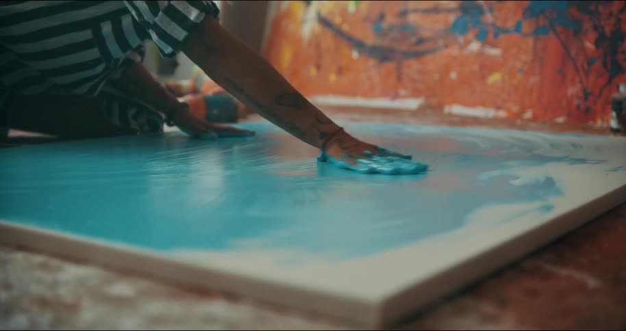 A woman is using the palms of her hands to rub blue paint all over a large canvas