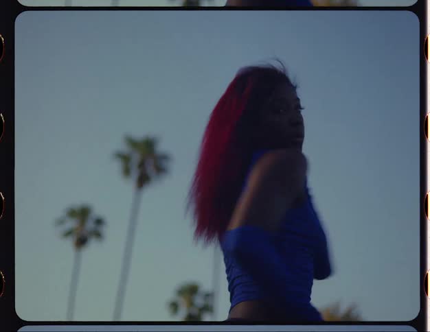 Female dancer with red hair blue top and sports pants dances on lawn in public park