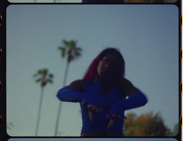 Woman with red hair blue top and sports pants dances on lawn in public park