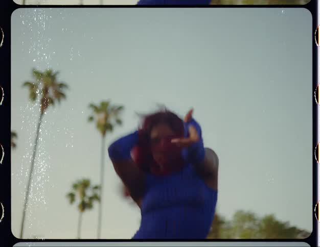 Footage with white scratches of a young woman with red hair dances in front of palm trees