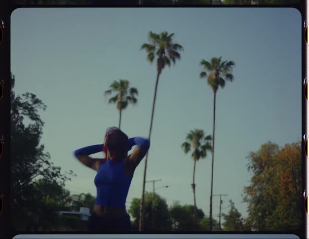 Female dancer moves through dance routine outdoors with homes and palm trees in the background