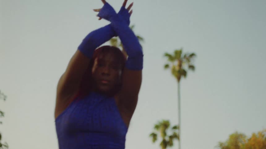 Female dancer with red hair blue top and sports pants dances on lawn in public park