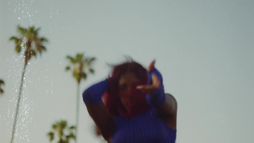 Young woman with red hair dances in front of palm trees caught on vintage film