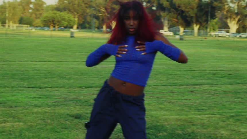 Woman with red hair blue top and sports pants dances on lawn in public park