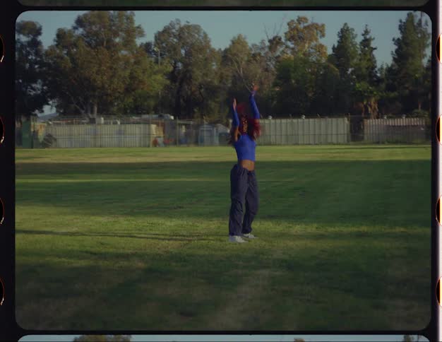 Young woman with red hair dances on a park at morning caught on vintage film