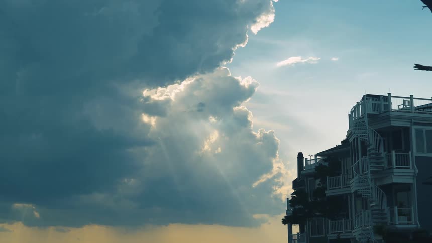 Sunlight shines through the clouds above a building with a balcony and spiral stairs leading to the roof