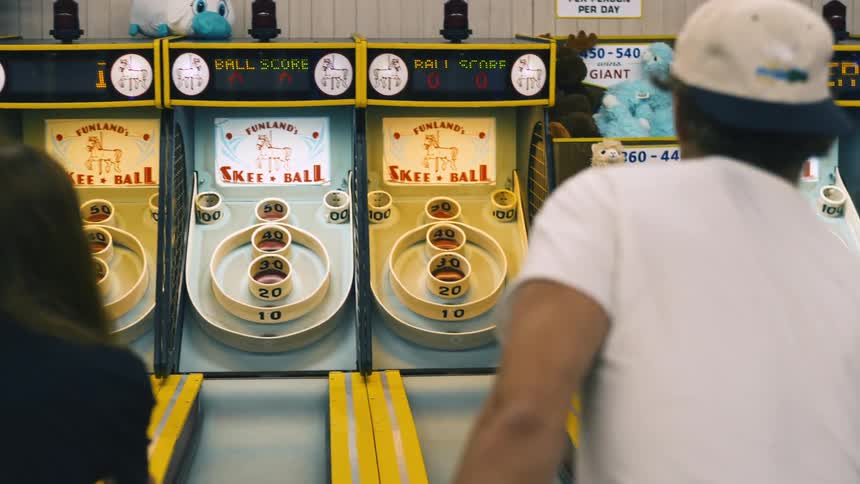 A man and a woman are in an arcade playing skee ball