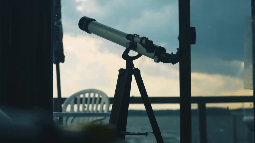 A telescope sits near a window overlooking the coast
