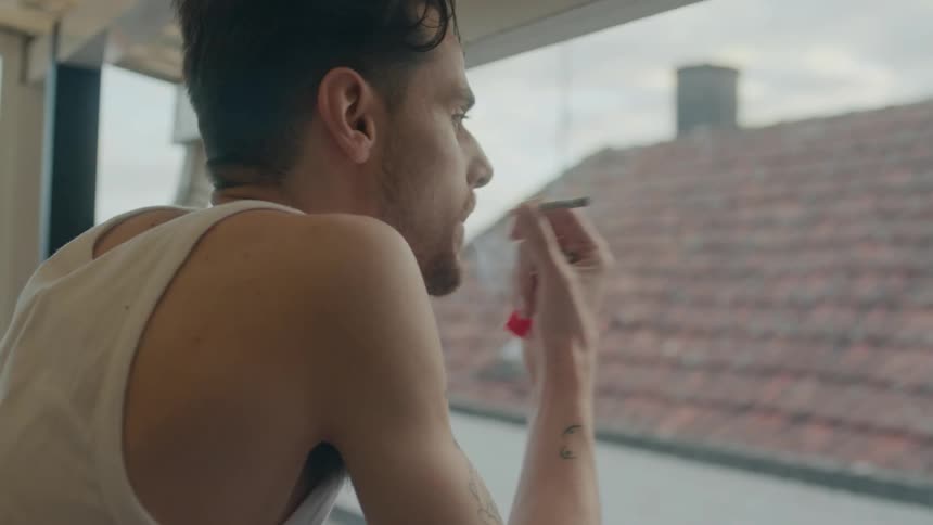 A man leans out his balcony while smoking a cigarette