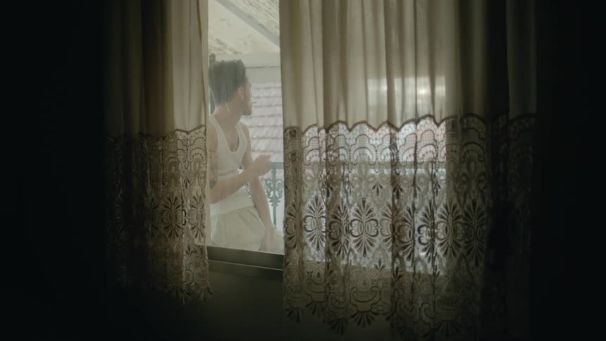 Man with white undershirt lights a cigarette on the balcony