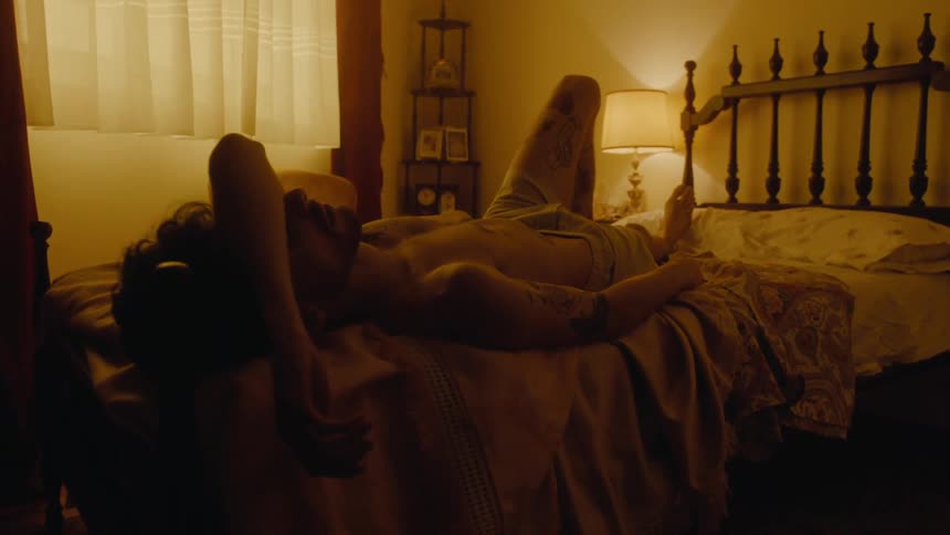 Shirtless man with shorts and tattoo lies on bed in bedroom
