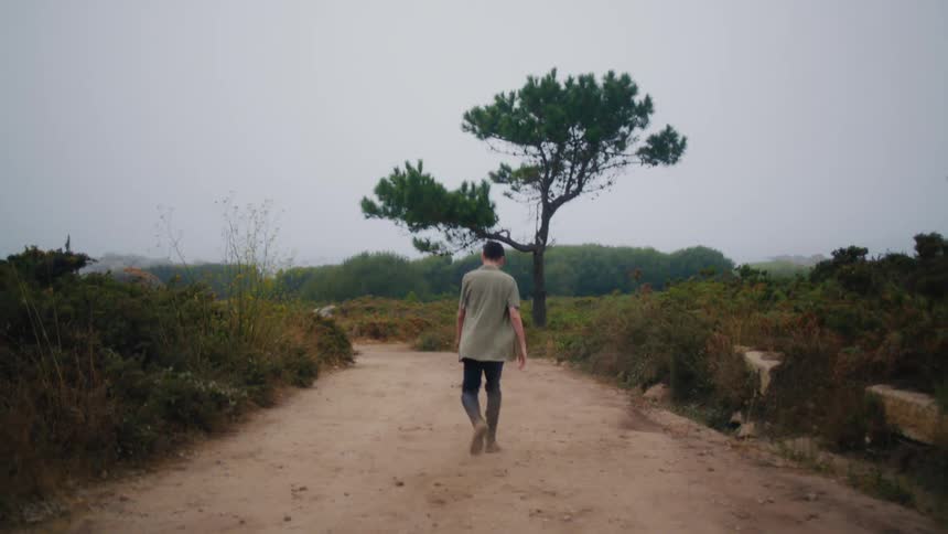 Angry man with olive drab shirt and pants walks on dirt road in the field