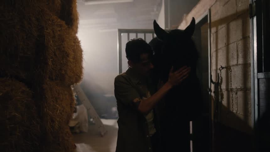 A man pets his horse while walking it through a stable