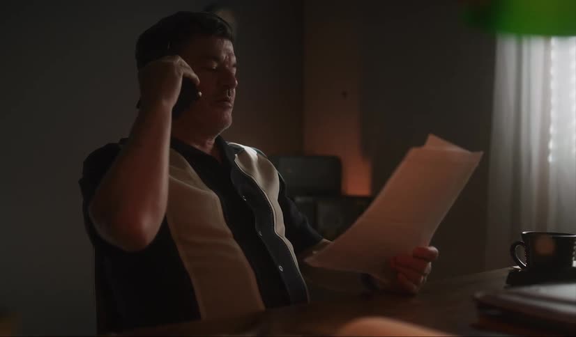 Middle aged man with black white shirt talks on smartphone while looking at papers in room