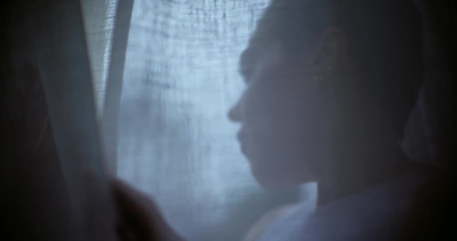 Seen through a curtain a woman looks out of a window