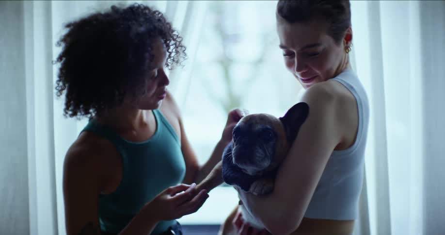Two friends are petting a puppy inside of there home