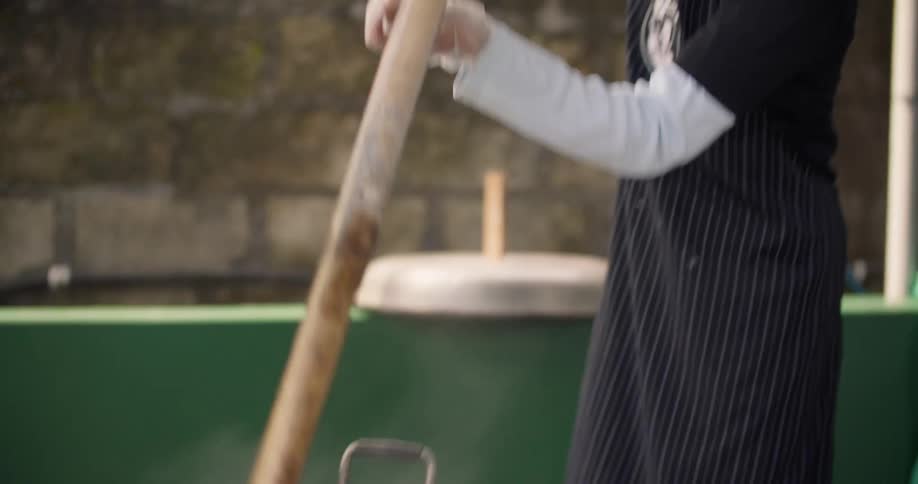 A woman is mixing food in large pots outside