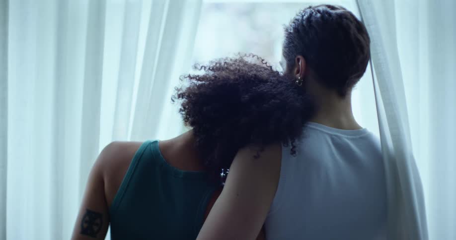 A young female couple embrace while looking out of the window