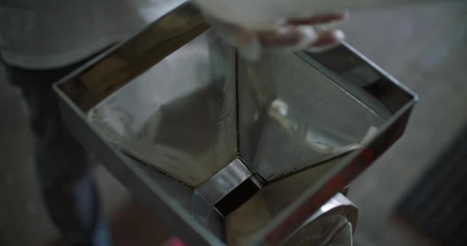 A person is pouring nuts into their hand and putting them into the funnel of a machine