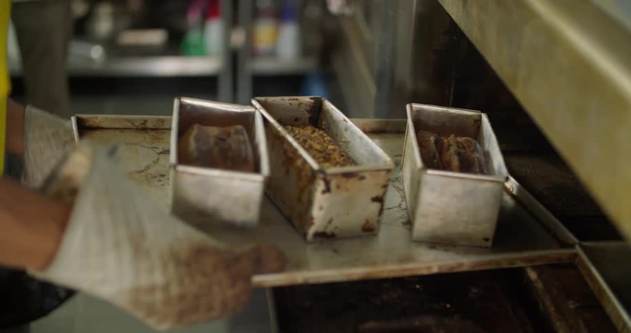 A man removes a tray of bread from the oven
