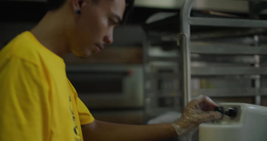 A young man uses a mixer in a bakery standing near racks