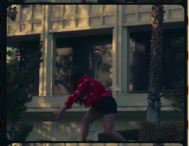 Young woman wearing a colorful jacket dancing outdoors in front of a building