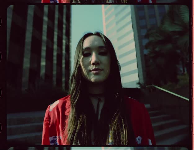 Close up of the face of a young woman wearing a colorful red jacket standing in front of buildings in the city