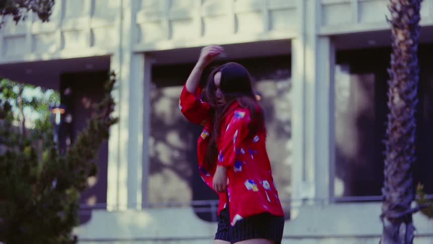Young woman wearing a colorful jacket dancing outdoors in front of a building