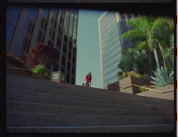 A woman dances at the top of a city plaza with buildings behind her