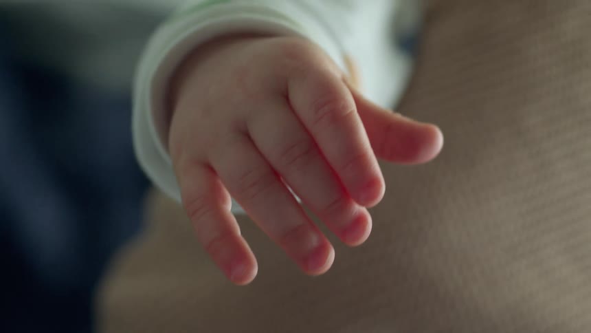 Sunlight shines on the hand of a baby as they are being held by their mother