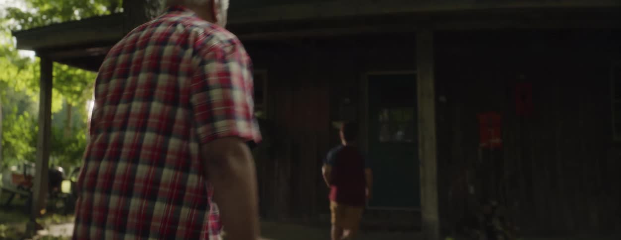 A little boy is running to the porch of a cabin and his grandfather is following him