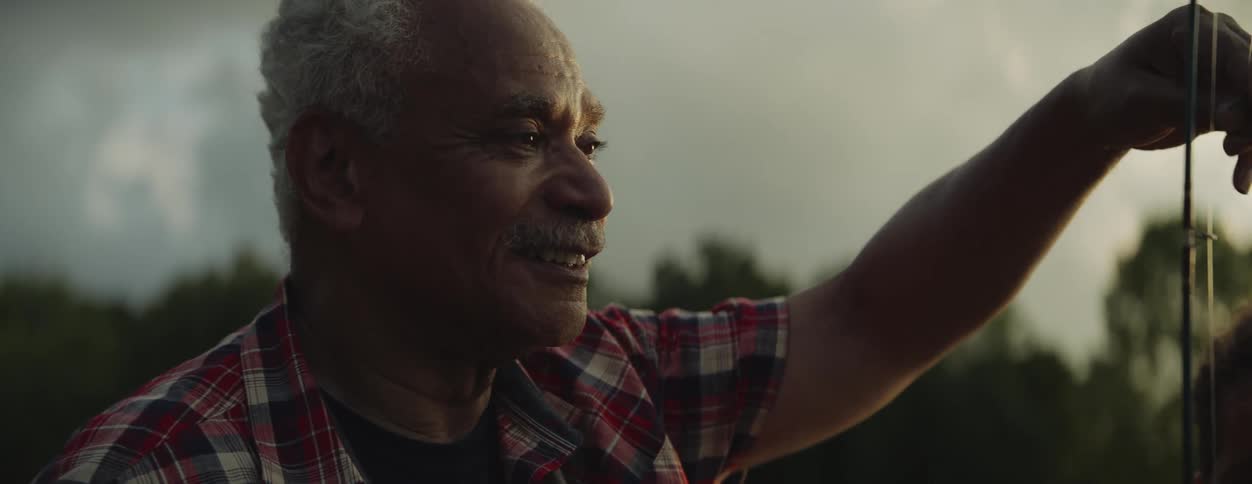 A man looks proudly at his grandson while holding up the fish on a line that he caught