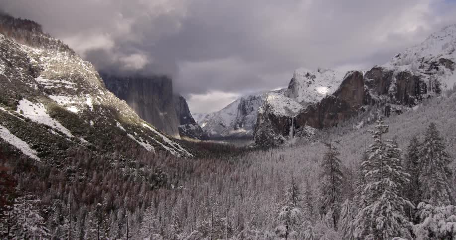A snow-covered valley surrounded by hills with clouds hovering above
