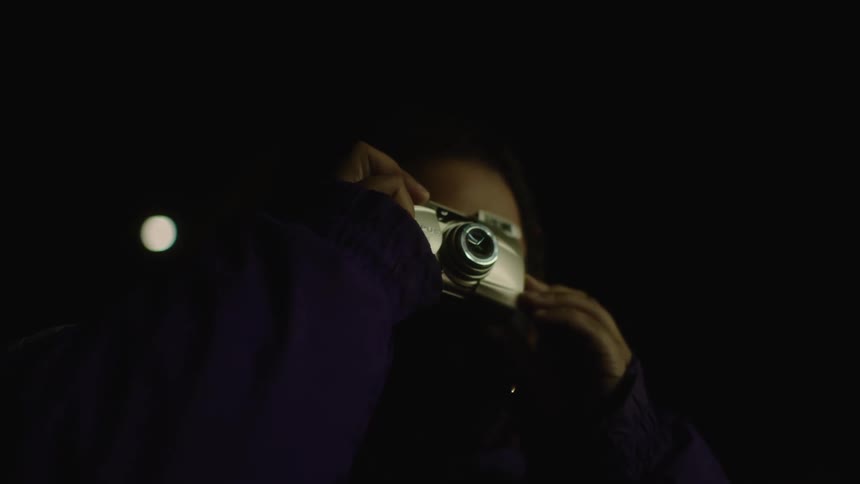 A woman is taking photos with a flash camera at night
