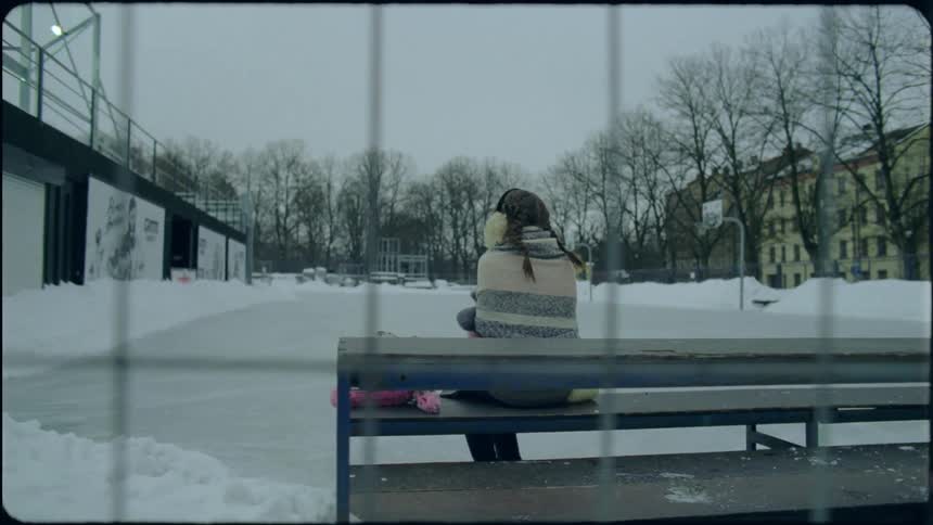 Woman sits on picnic table near iced basketball court with apartments in background