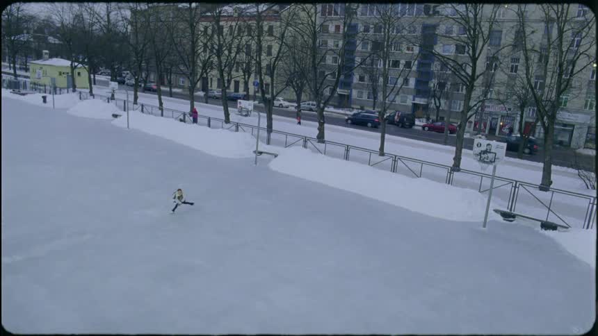 A woman figure skating on an outdoor rink in a park near a busy street