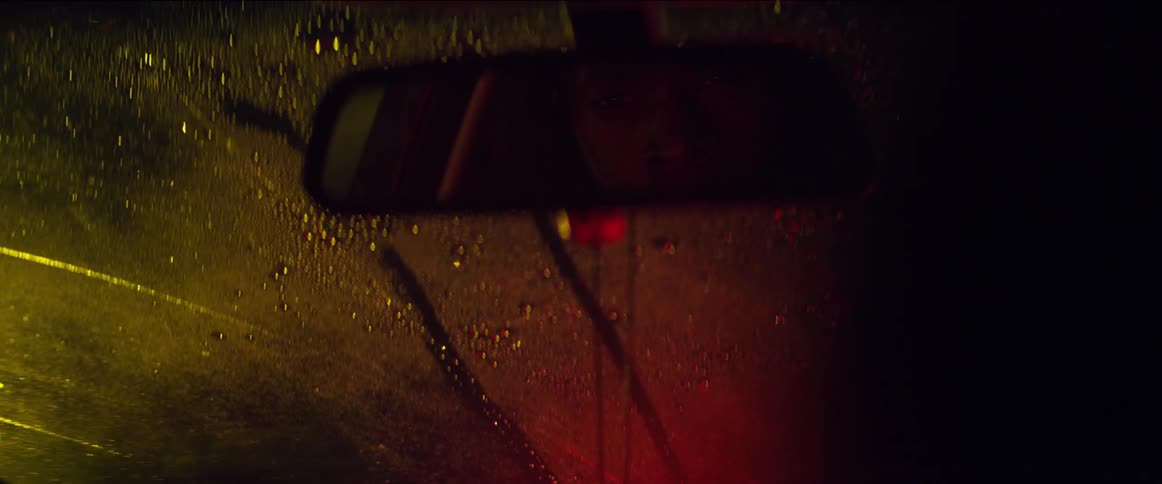 A driver looks in the rearview mirror then turns his head to look back on a rainy night