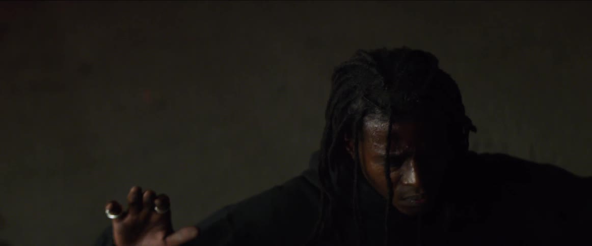 A black man with dread locks is sitting down as he raises his hands in the air