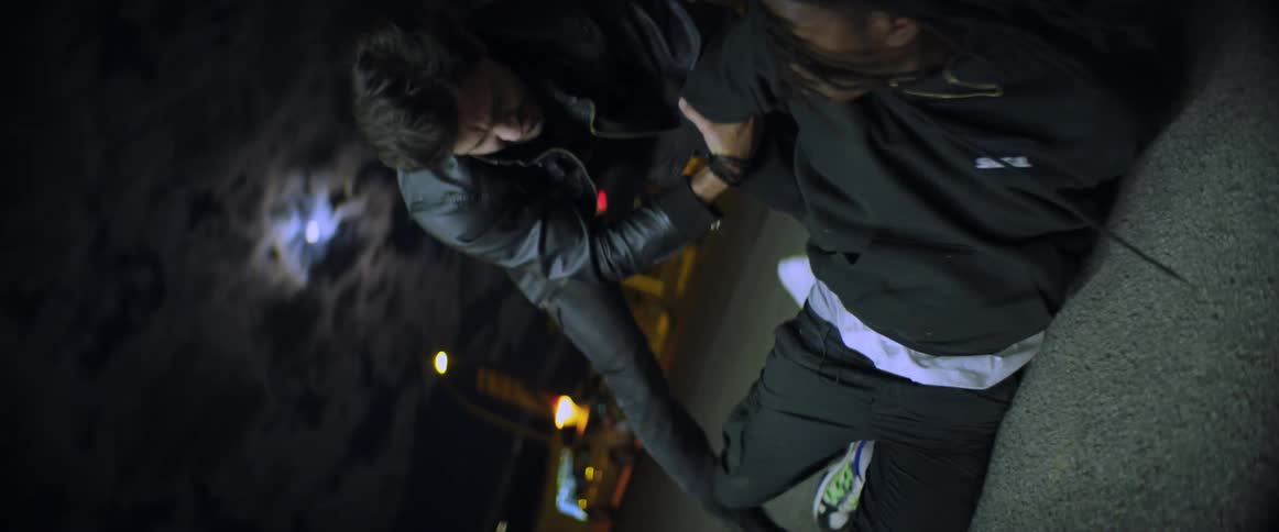A young man lying on the parking lot ground face down is handcuffed and hauled up by a police officer