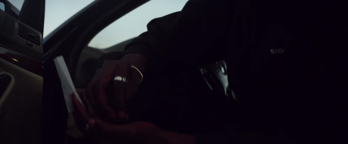 A man reads a piece of paper while sitting in his car with the door open
