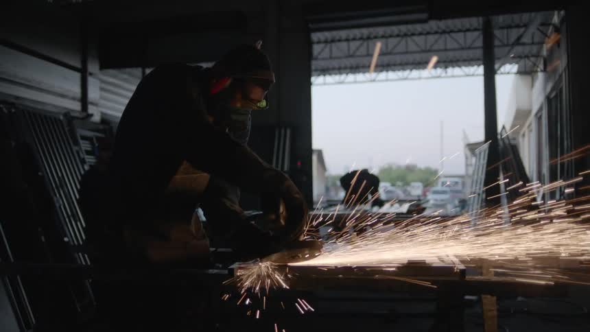 A man stands over metal he is working with and holding a machine as sparks fly