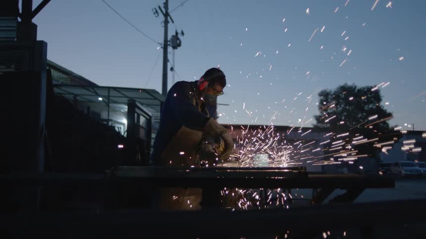 Man wearing protective gear polishes metal outdoors and creates a shower of sparks